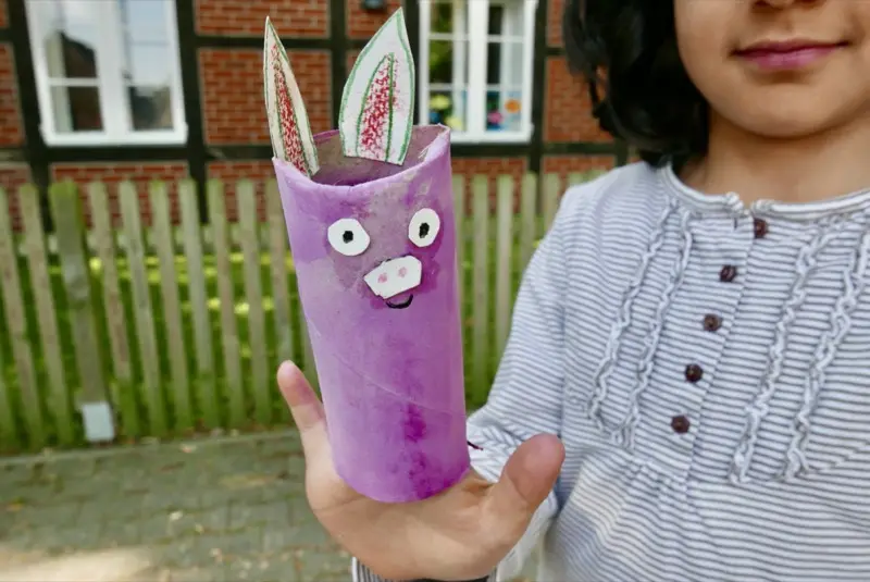 Kind zeigt stolz eine selbst gebastelte Figur aus einer Papprolle